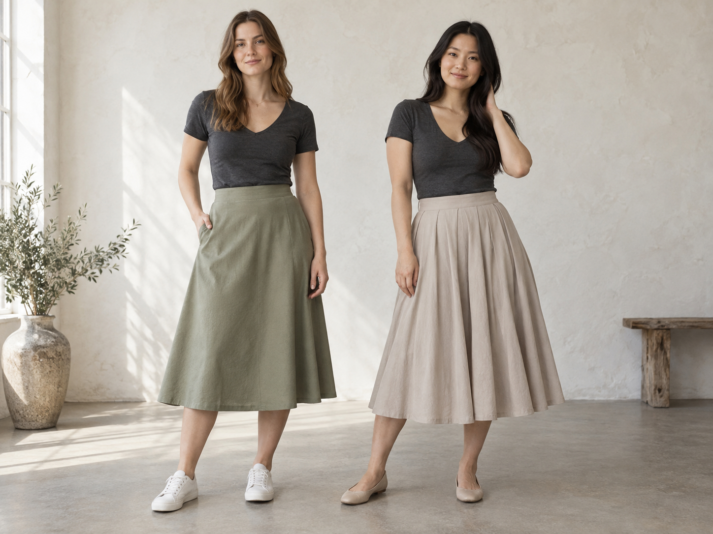 Two women in charcoal V-neck tops, one wearing a sage A-line skirt and the other a fuller pleated stone skirt.